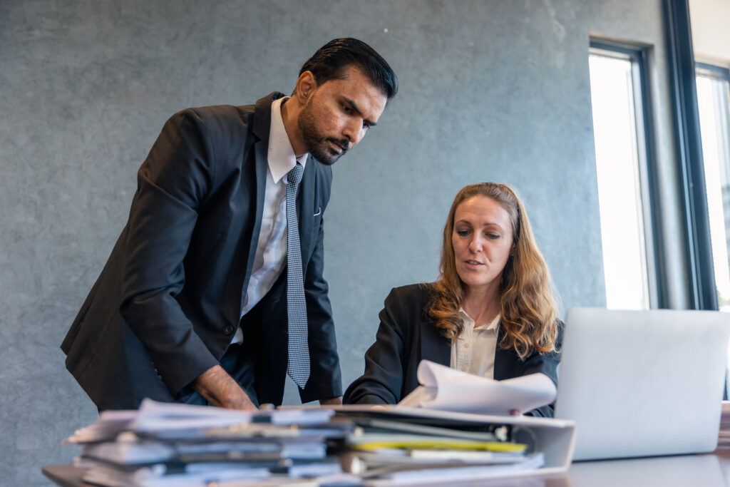 Two legal professionals in business attire reviewing case documents together at a desk, symbolizing the collaboration between a lawyer and a paralegal.