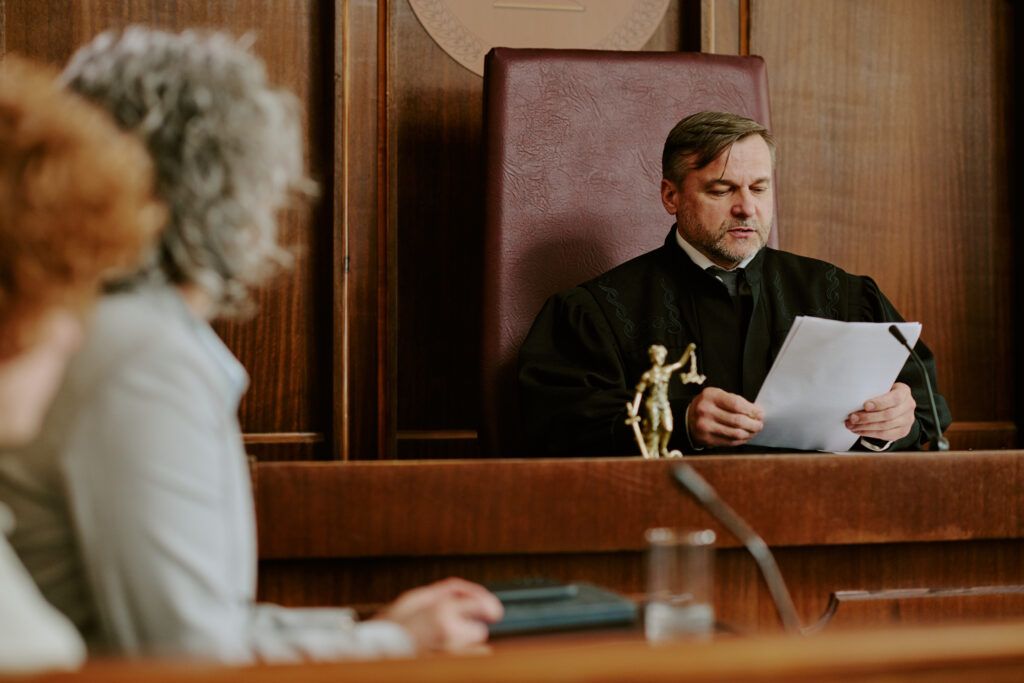 Male judge seated in a courtroom reading legal documents with two blurred figures in the foreground, symbolizing courtroom procedures and judicial review
