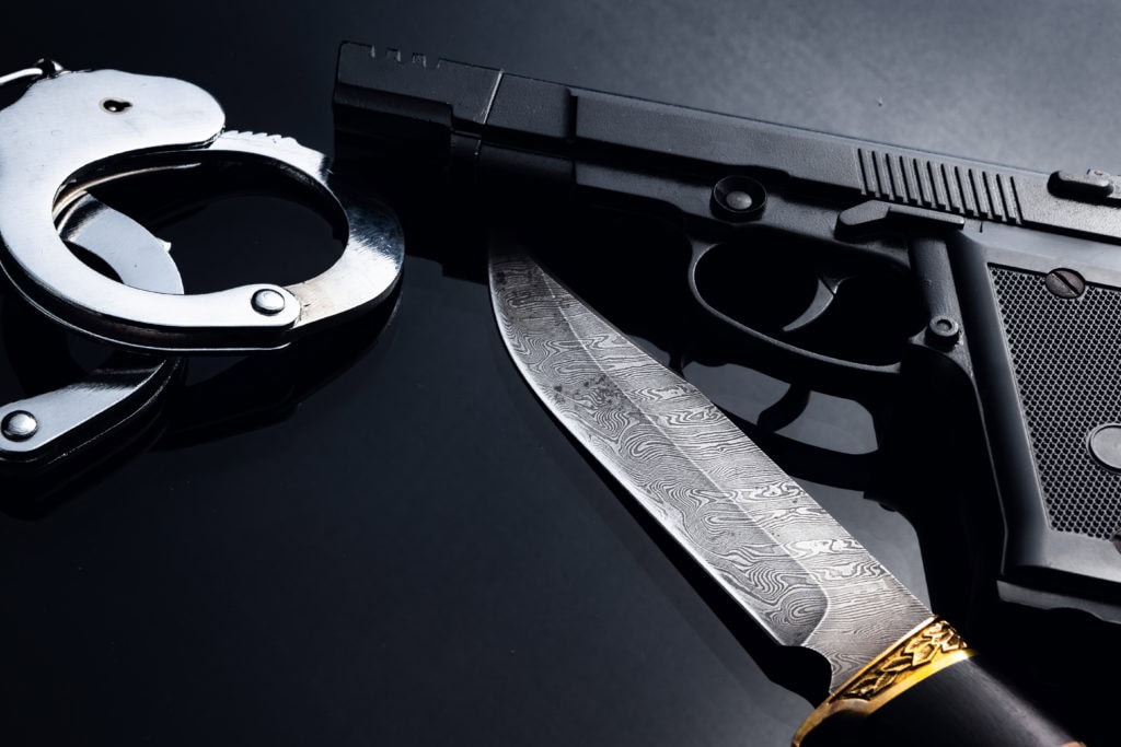 Criminal Charges Due To Carrying A Weapon Gun, knife and handcuffs on black background