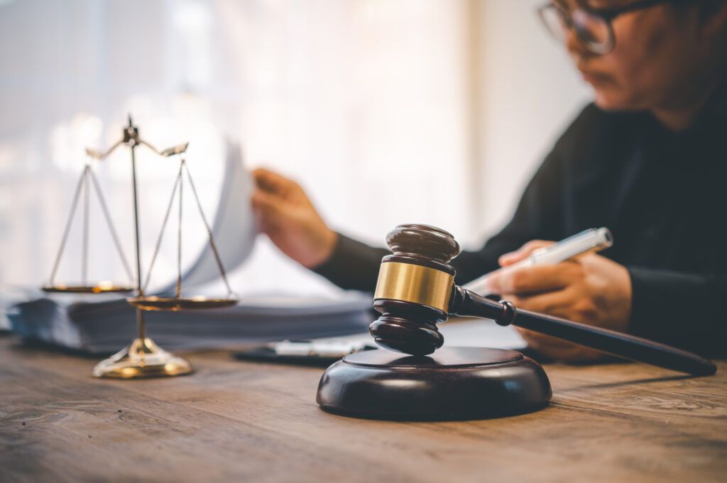 Judge examining legal documents at a wooden desk with a gavel and golden justice scales in the foreground, symbolizing criminal court proceedings