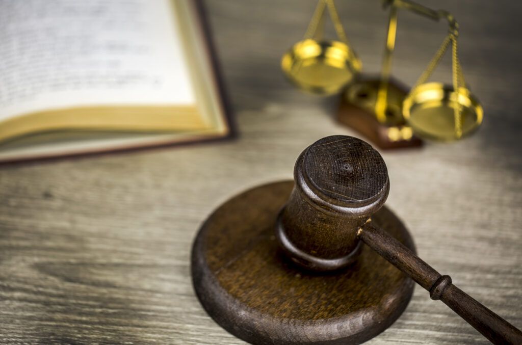 Judge's wooden gavel next to a blurred law book and golden scales of justice on a courtroom desk, representing legal decisions and judicial authority