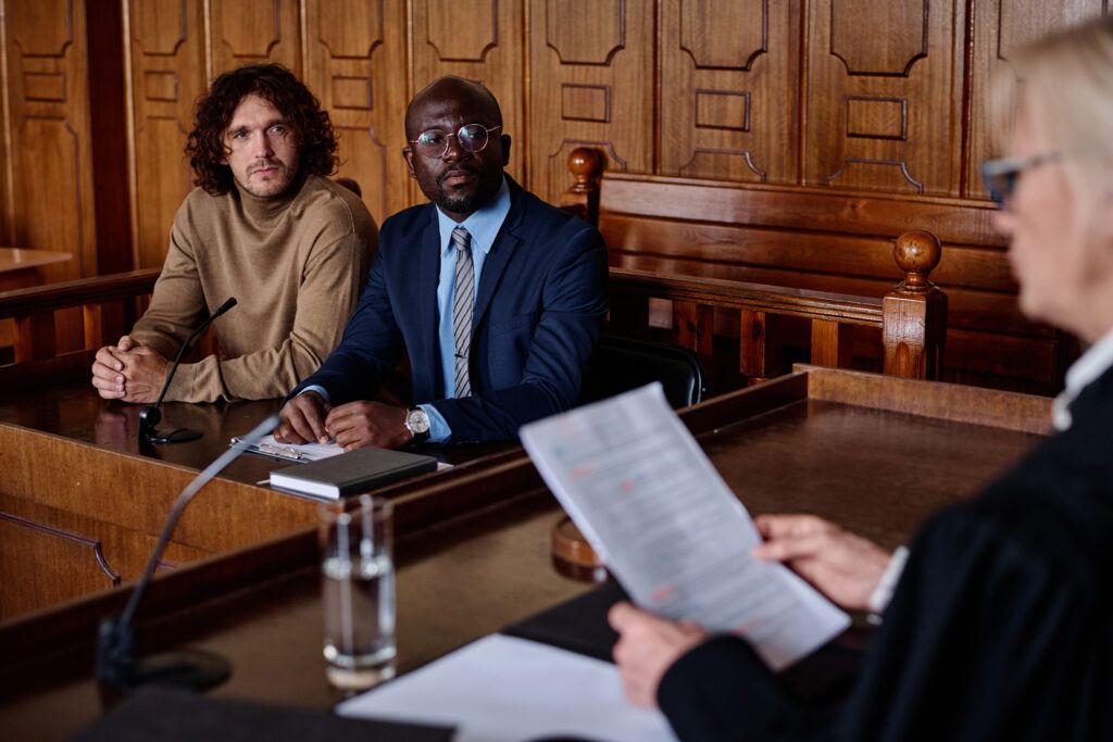Criminal defence lawyer seated beside a client in court while listening to proceedings involving a guilty plea or contested evidence.