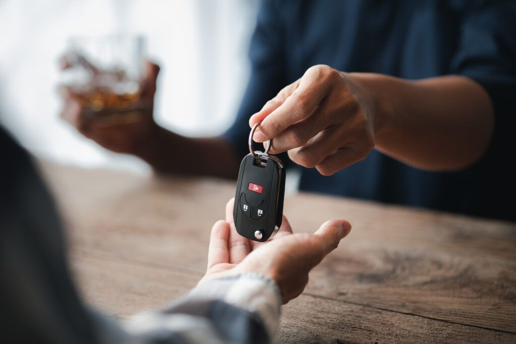 Person handing over car keys while holding a drink, representing impaired driving risks during the holiday season