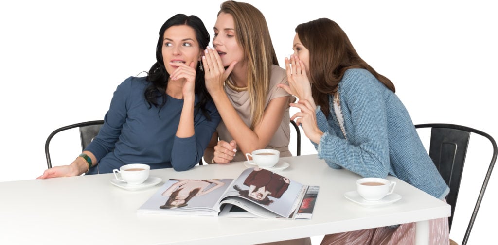 three women sitting at a table whispering to each other