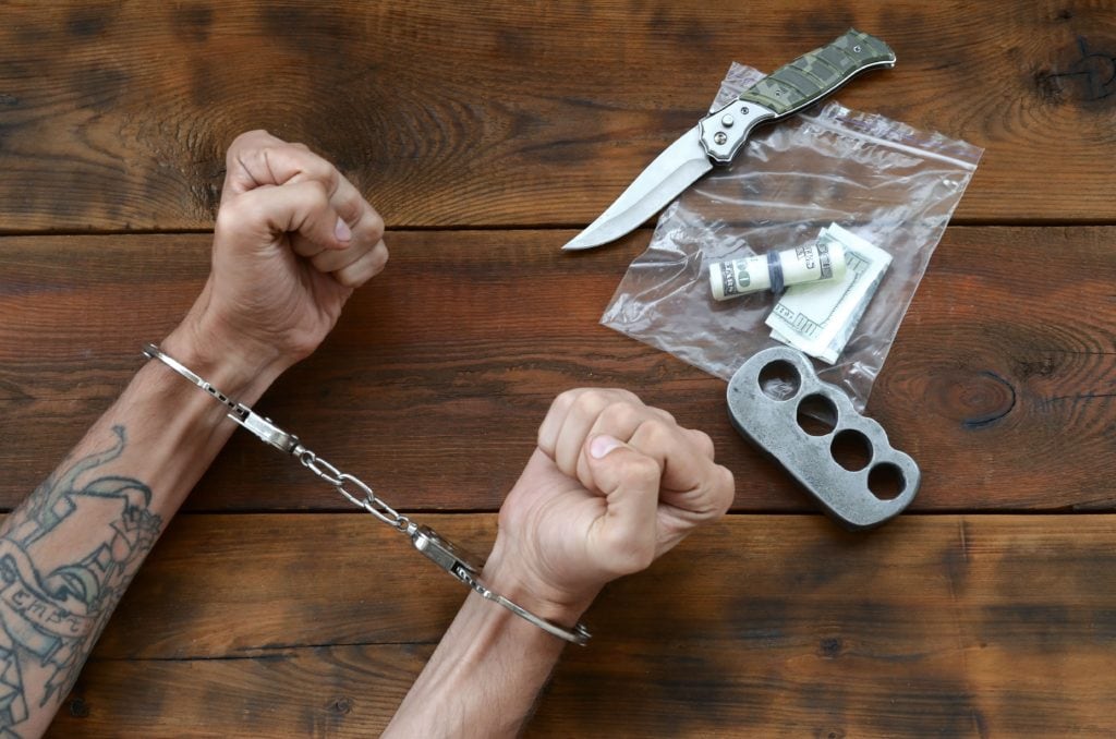 Cuffed hands of tattooed criminal suspect and plastic ziplock packet of evidence for investigation
