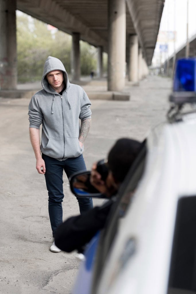 policeman looking on hooded young man on street out of window