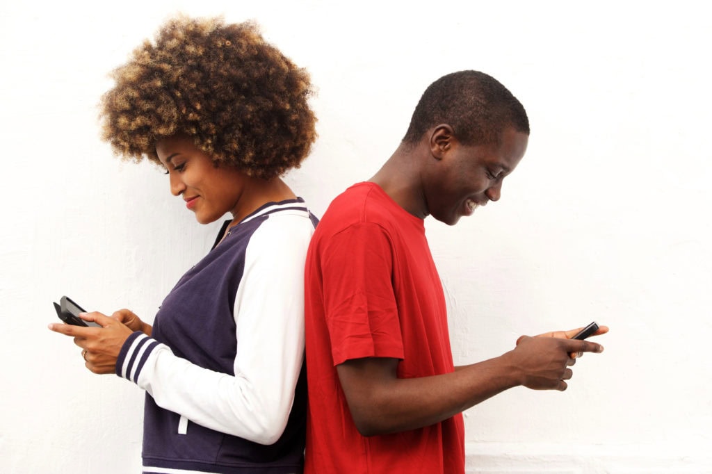 african couple standing back to back holding mobile phones