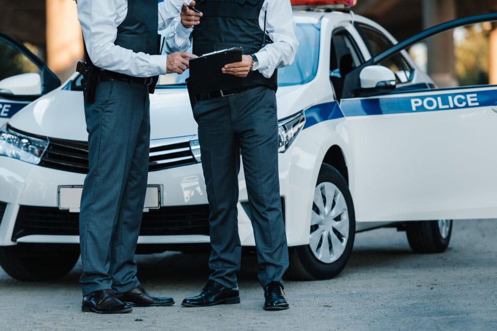 partial view of male police officer with clipboard and pointing by finger to colleague standing near