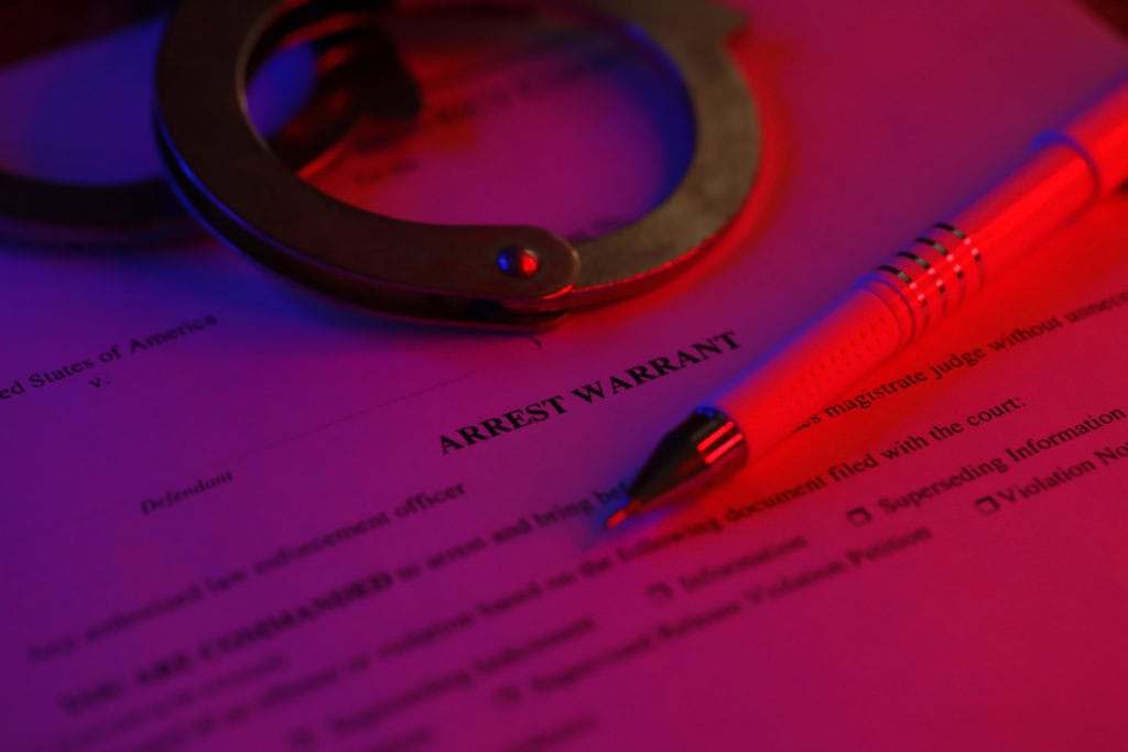 District Court Arrest Warrant court papers with handcuffs and blue pen on United States flag. Concept of permission to arrest
