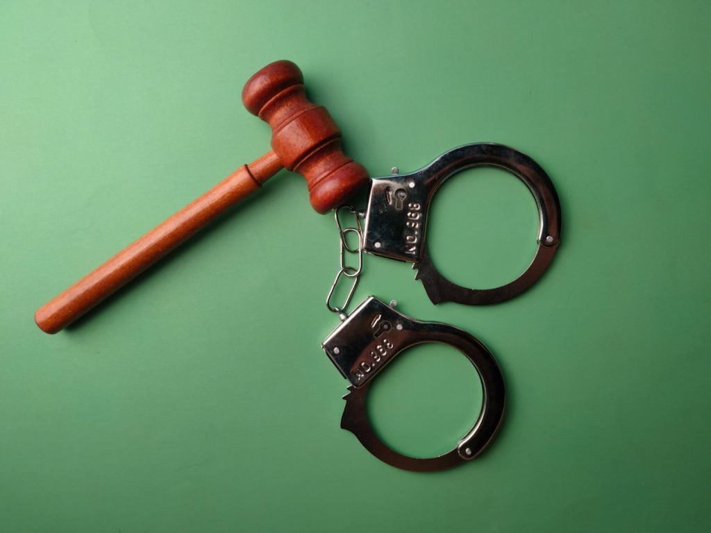 Top view metal handcuff and wooden gavel on a green background