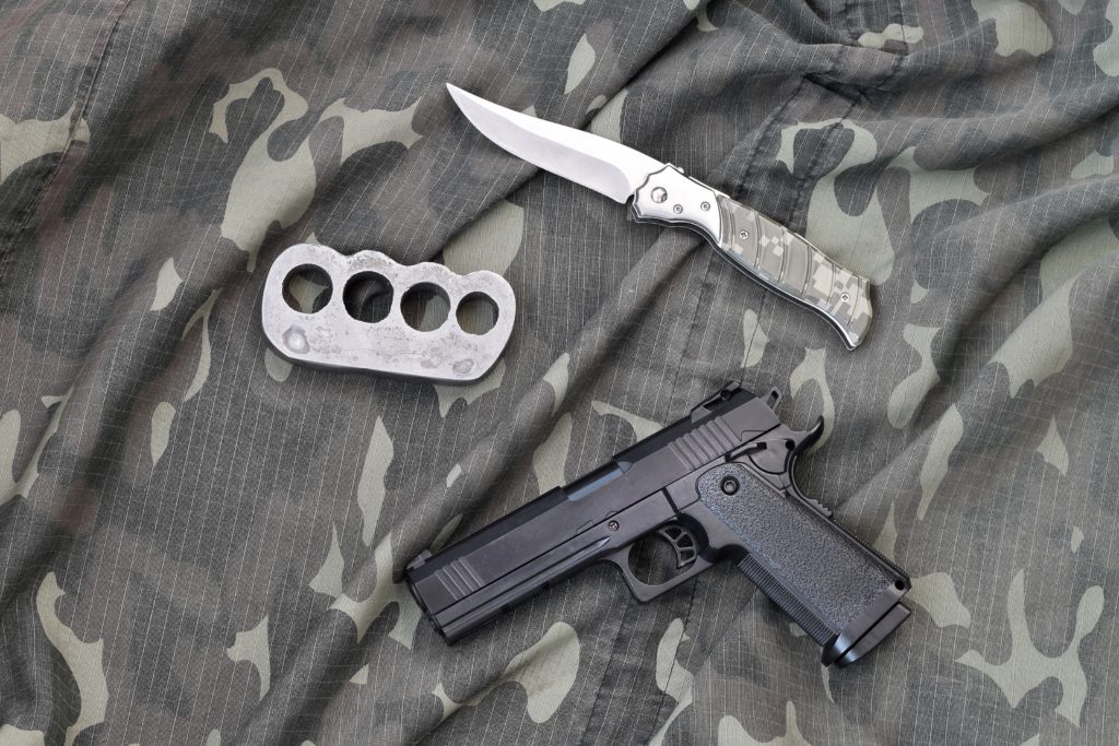 Handgun lies with brass knuckles and knife on camouflage military uniform close up. Concept of looting and arms trade