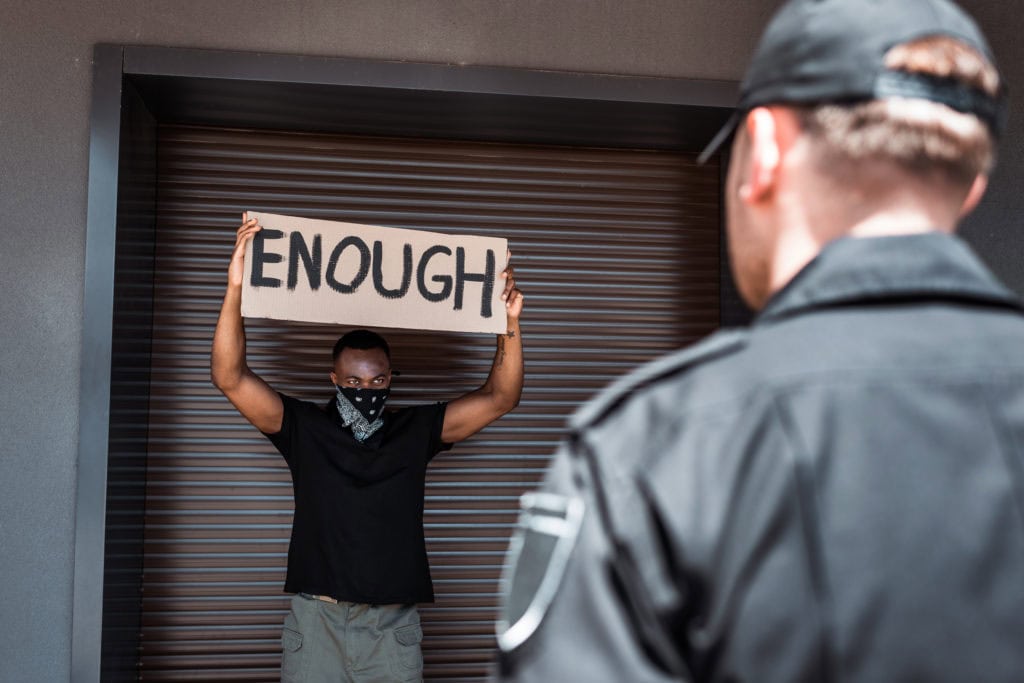 selective focus of african american man with scarf on face holding placard with enough lettering