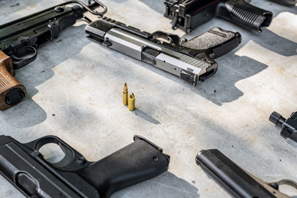 Multiple pistols and bullets arranged on a table, highlighting firearm types and ammunition used in discussions about gun laws in Canada