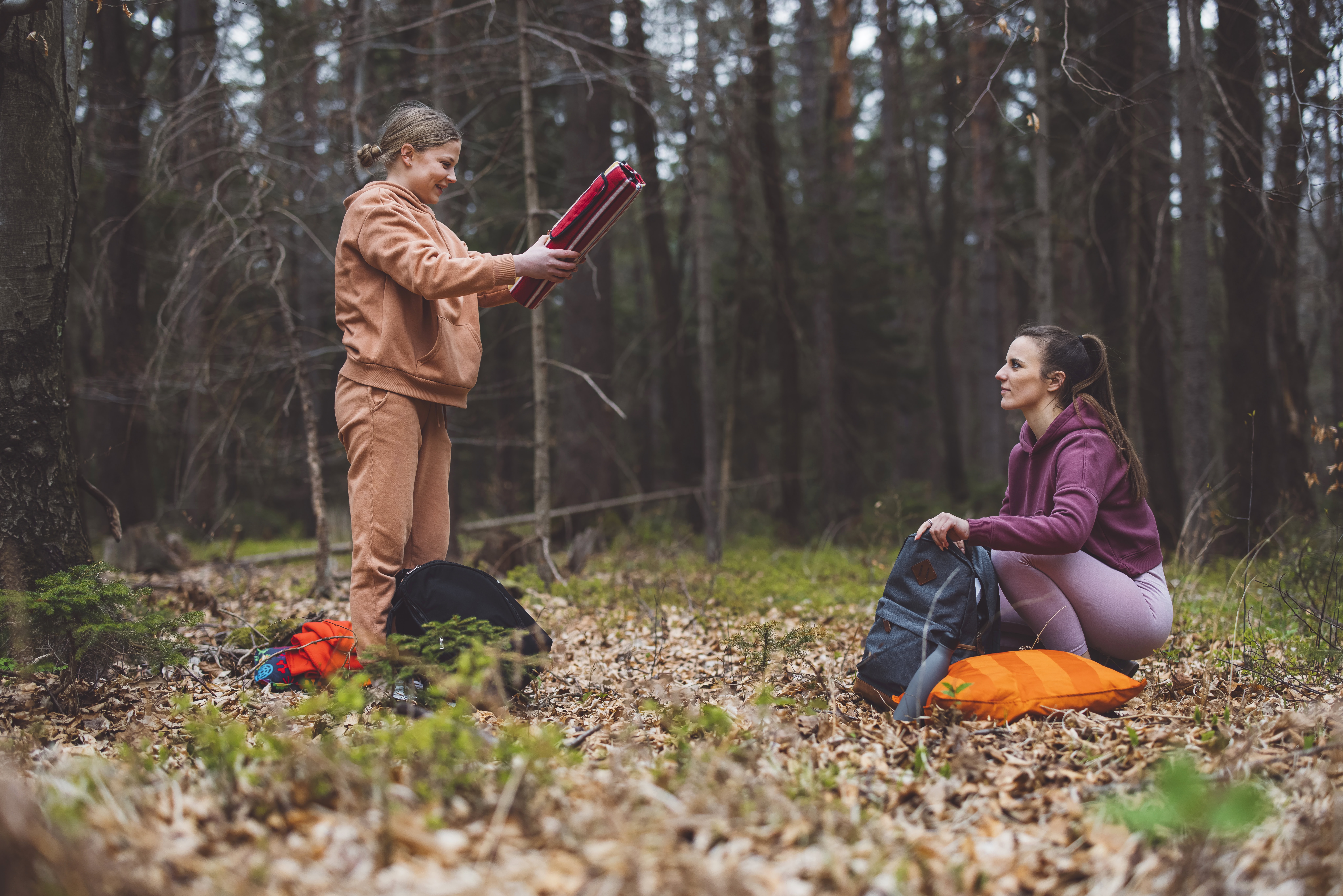 Two young women sitting on a blanket in a forest having picnic, one is looking at a smartphone while