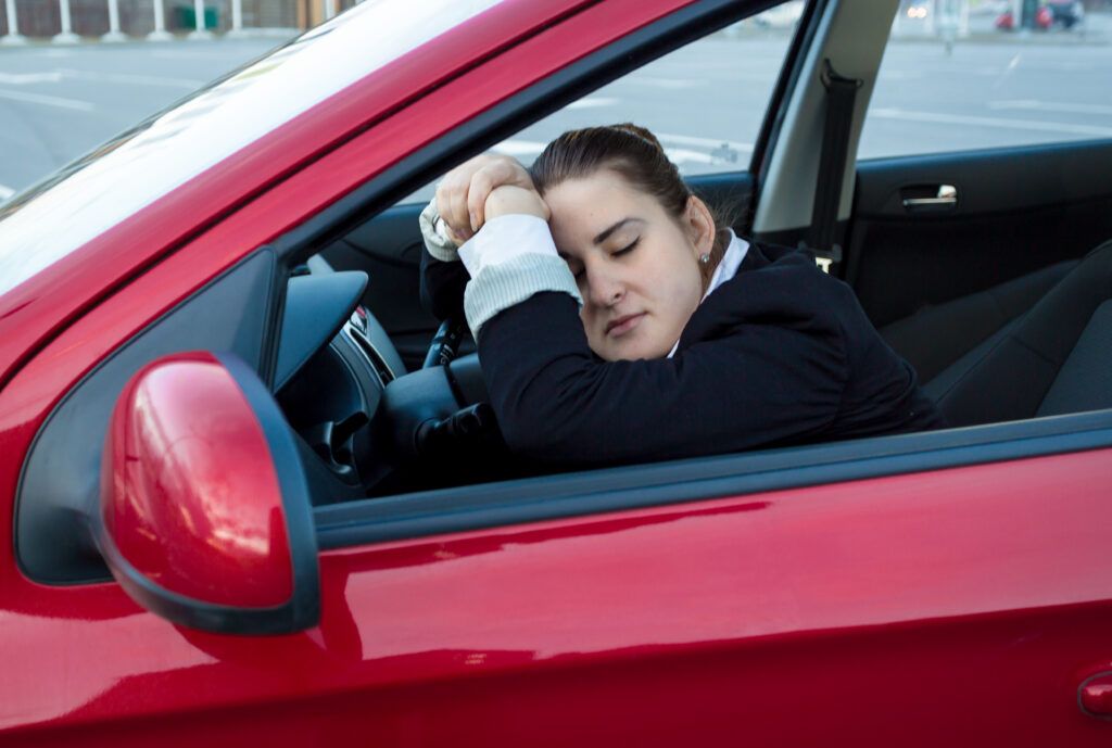 Woman sleeping in the driver’s seat of a parked car, highlighting the legality of sleeping in your car in Canada