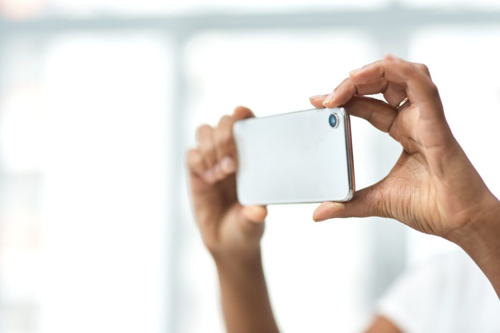 Close-up of a person holding a smartphone to record, highlighting privacy concerns and legal issues related to unauthorized video recording in Canada