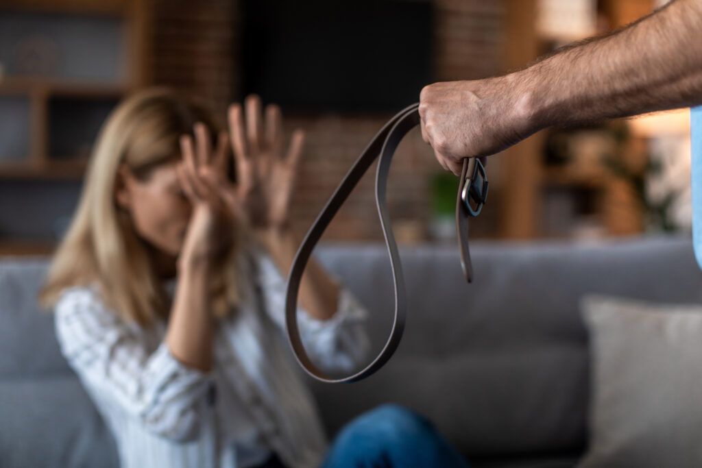 Person holding a belt while a woman raises her hands defensively, illustrating the legal distinction between domestic violence and assault in Canada.